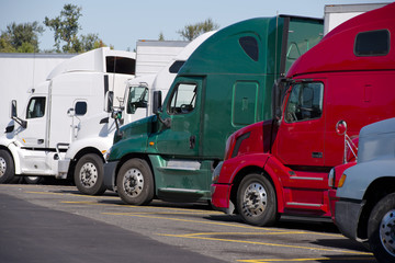 Different make and moders of big rigs semi trucks stand in row on truck stop