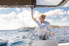 Attractive Blond Female Skipper Navigating The Fancy Catamaran Sailboat On Sunny Summer Day On Calm Blue Sea Water. Luxury Summer Adventure, Active Nautical Vacation.