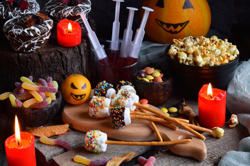 Halloween trick or treat party. Funny delicious sweets and pumpkin on wooden background - muffins, cupcakes, marshmallows, popcorn, juice, jellies, candy.