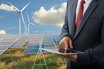 Businessman holding a tablet at Solar panels with wind turbines  blue sky with clouds background and (solar cell)  create the clean electric power Business Concept.