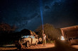 © zephyr_p - Young male traveler using flashlight crossing the southern milky way at campsite in Namibia, Africa. Road trip travel with stargazing concepts