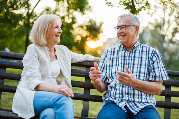 Two happy seniors are sitting and talking in park. 