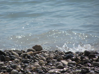 The shore of the sea close-up: a pebble from a pebble with sand and an incident wave. Beautiful background.