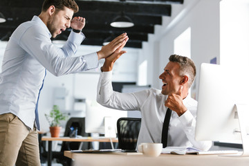 Fototapete - Photo of happy businessmen 30s in formal clothes giving high five together in office, during successful deal