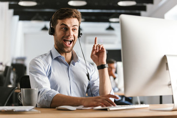 Fototapete - Photo of caucasian worker man 20s wearing office clothes and headset, working on computer in call center