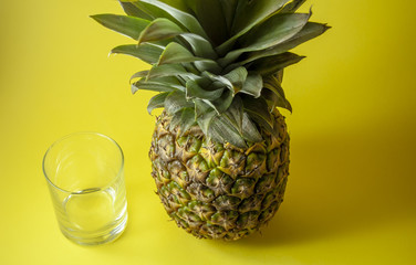 Single pineapple isolated on yellow background with empty glass.