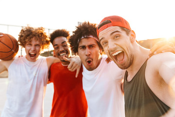 Wall Mural - Photo closeup of young sporty men smiling and taking selfie, while playing basketball at playground outdoor during summer sunny day