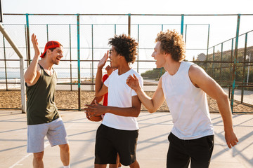 Wall Mural - Portrait of multiethnic sporty men playing basketball at the playground outdoor, during summer sunny day