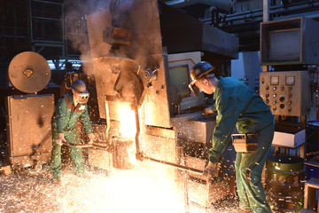 Industriearbeiter in einer Giesserei beim Abstich vom Schmelzofen zur Weiterverarbeitung // Industrial worker in a foundry - teamwork