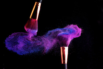 Make-up brush with colorful powder splashes explosion on black background