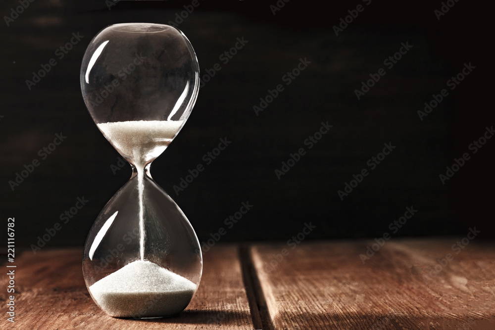 A side view of an hourglass with falling sand, on a dark background with copy space - obrazy, fototapety, plakaty 