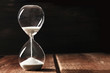 A side view of an hourglass with falling sand, on a dark background with copy space