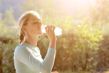  Young sporty woman after workout and running drinks water on a sunny day