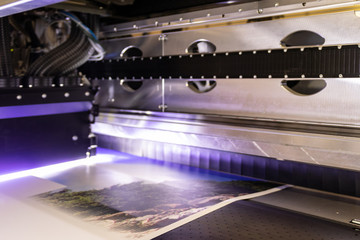 Massive, big printer. Professional press machinery, armed with special, glossy, vinyl rolls. Large print head in motion.