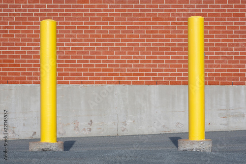 Fotografía Yellow traffic bollards in front of brick building wall.