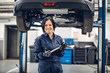 Auto car repair service center. Happy female mechanic standing by the car