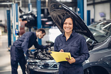 Auto Car Repair Service Center. Two Mechanics - Man And Woman Examining Car Engine