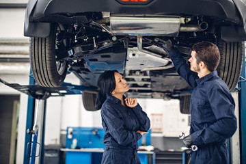 Wall Mural - Auto car repair service center. Two mechanics - man and woman examining car