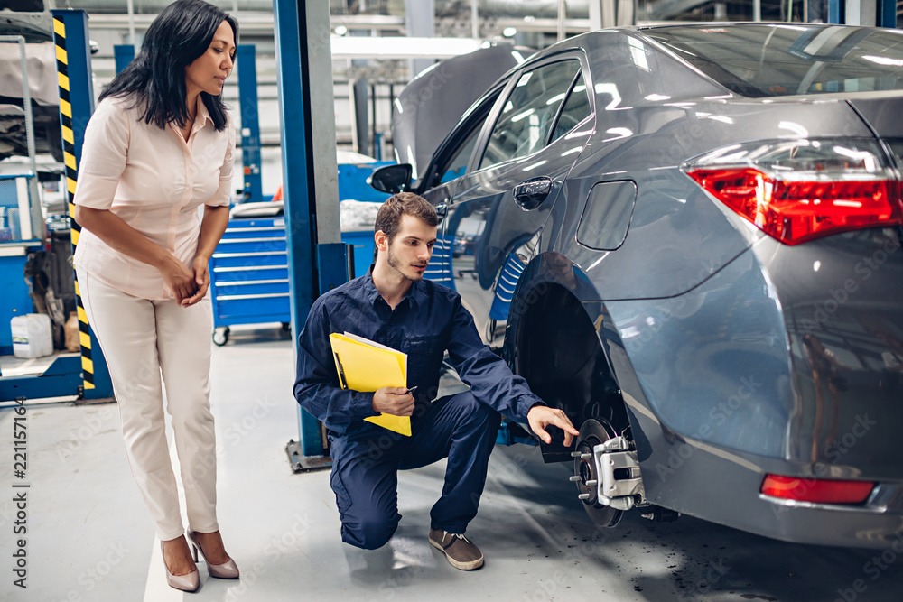 Auto car repair service center. A female customer and mechanic checking car breaks