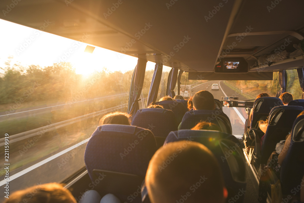 Background. Travel by bus. Bus interior. Salon of the bus with people fill the sun with light in the sunset. People travel on a big tourist bus. The bus rides along the mornings in the sunrise - obrazy, fototapety, plakaty 