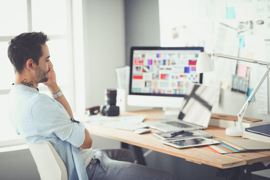 Portrait of young designer sitting at graphic studio in front of laptop and computer while working online.