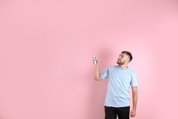 Wall Mural - Young man with air conditioner remote on color background, copy space text