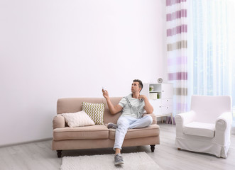 Canvas Print - Young man operating air conditioner with remote control at home