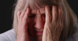 Fototapeta Kosmos - Tight shot of elderly woman with migraine headache rubbing head on gray backdrop