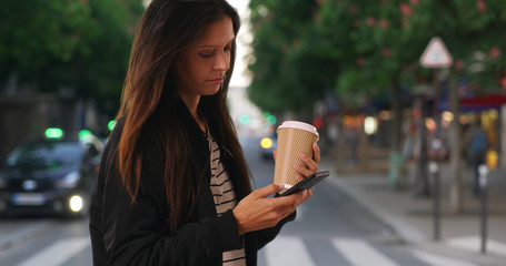 Wall Mural - Millennial female with her coffee texting with cell phone while on city street