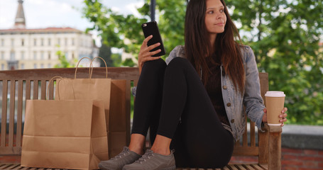 Wall Mural - Hipster millennial female in jean jacket sitting on park bench texting