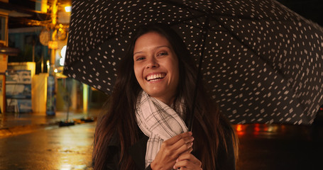 Wall Mural - Happy millennial female on city street at night holding umbrella