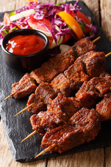 Nigerian spicy suya kebab on skewers with fresh vegetable salad and ketchup close-up. vertical