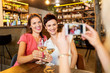© Syda Productions - people, technology and lifestyle concept - woman photographing friends drinking wine by smartphone at bar or restaurant