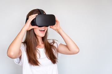 Smiling positive woman wearing virtual reality goggles headset, vr box. Connection, technology, new generation, progress concept. Girl trying to touch objects in virtual reality. Studio shot on gray