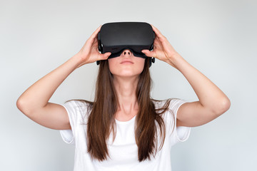 Wall Mural - Young woman wearing virtual reality goggles headset, vr box. Connection, technology, new generation, progress concept. Girl trying to touch objects in virtual reality. Studio shot on gray