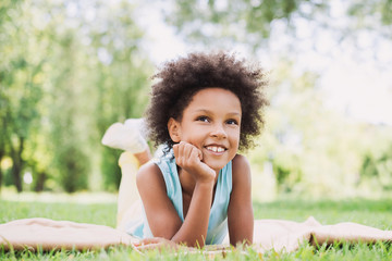 Wall Mural - Beautiful kid girl lying down in a grass.  Healthy smiling little girl enjoying life.  Relaxing in nature, summer holidays concept