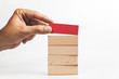 Hand put red wooden block on the stack of wooden blocks