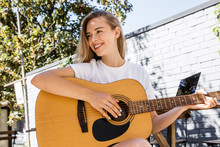 Young Hipster Woman Sitting In Grass And Playing Guitar On Park Or Garden Background. Teen Girl Learning To Play Song And Writing Music. Hobby, Lifestyle, Relax, Instrument, Leisure, Education Concept