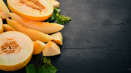 Fresh melon Sliced to pieces of melon. On a black wooden background. Free space for text. Top view.