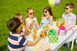 © Syda Productions - holidays, childhood and celebration concept - happy kids in sunglasses sitting at table on birthday party at summer garden and eating cupcakes