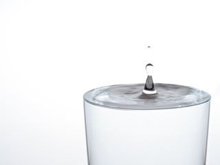 drop of water, about to make the glass overflow and run over. on white.