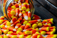 Halloween Theme Featuring A Spilling Of Candy Corn From A Jar Not A Wooden Table.