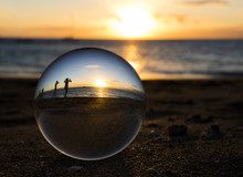 People In Silhouette On Beach At Sunset Through Glass Ball