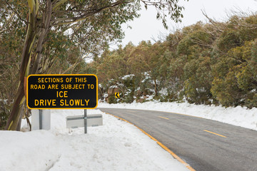 Winter road in Australian alps ice on road yellow lane marking Drive Slowly warning sign