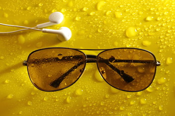 Wall Mural - earphone sunglasses from sun water drop on abstract yellow background. melodies of autumn.