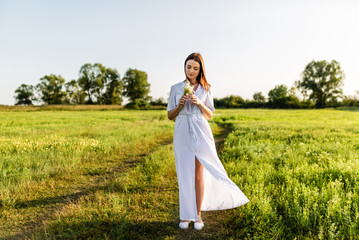 Wall Mural - attractive young woman in white dress with field flowers bouquet on green field