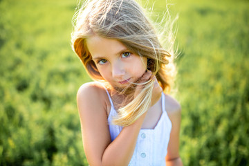 Wall Mural - close-up portrait of cute little child in white dress posing in green field and looking at camera