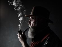 Dramatic Portrait Of Senior Man In Hat Smoking Tobacco Pipe. Profile View Of Austrian, Tyrolean, Bavarian Old Man