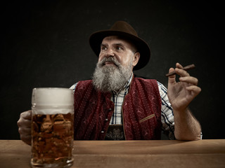 Germany, Bavaria, Upper Bavaria. The smiling man with beer dressed in in traditional Austrian or Bavarian costume in hat holding mug of beer at studio