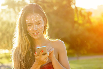 model woman long-haired in red dress holds phone and talking typing text with boyfriends in hand rays of sun background . enamored girl chating with friends in the park, concept face id